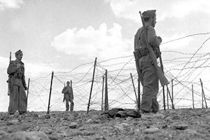 Soldados españoles de infantería patrullan frente a la valla defensiva de una ciudad del Sáhara, probablemente El Aaiún, en los años 1957-1958.
