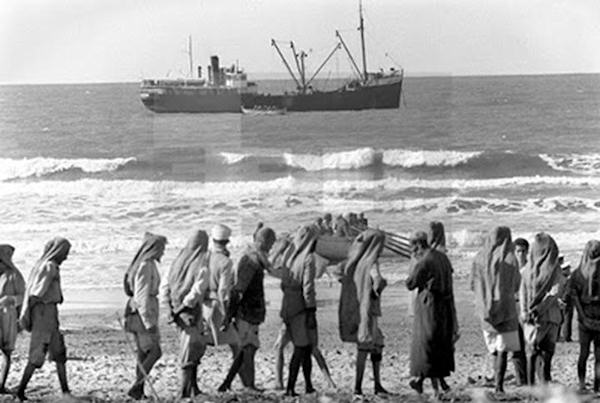 Operación de desembarco en la playa de Sidi Ifni. Los porteadores nativos esperan la llegada del carabo con la mercancía desembarcada del barco fondeado.