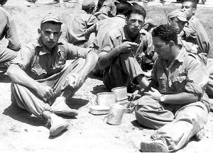 Los soldados comiendo en el suelo a pleno sol.